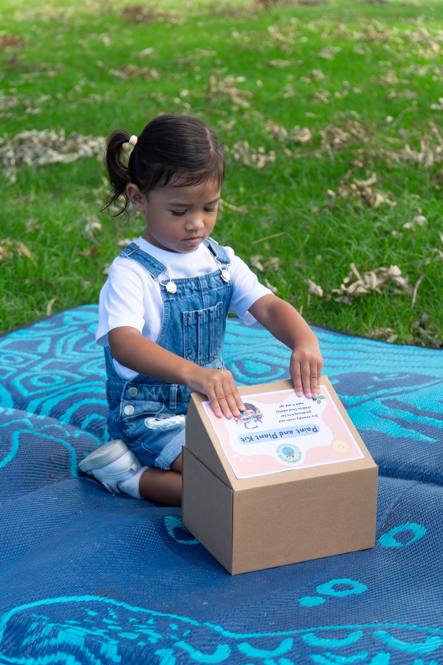 A young girl in overalls is opening her EnviroMentoring Paint and Plant DIY Kit.