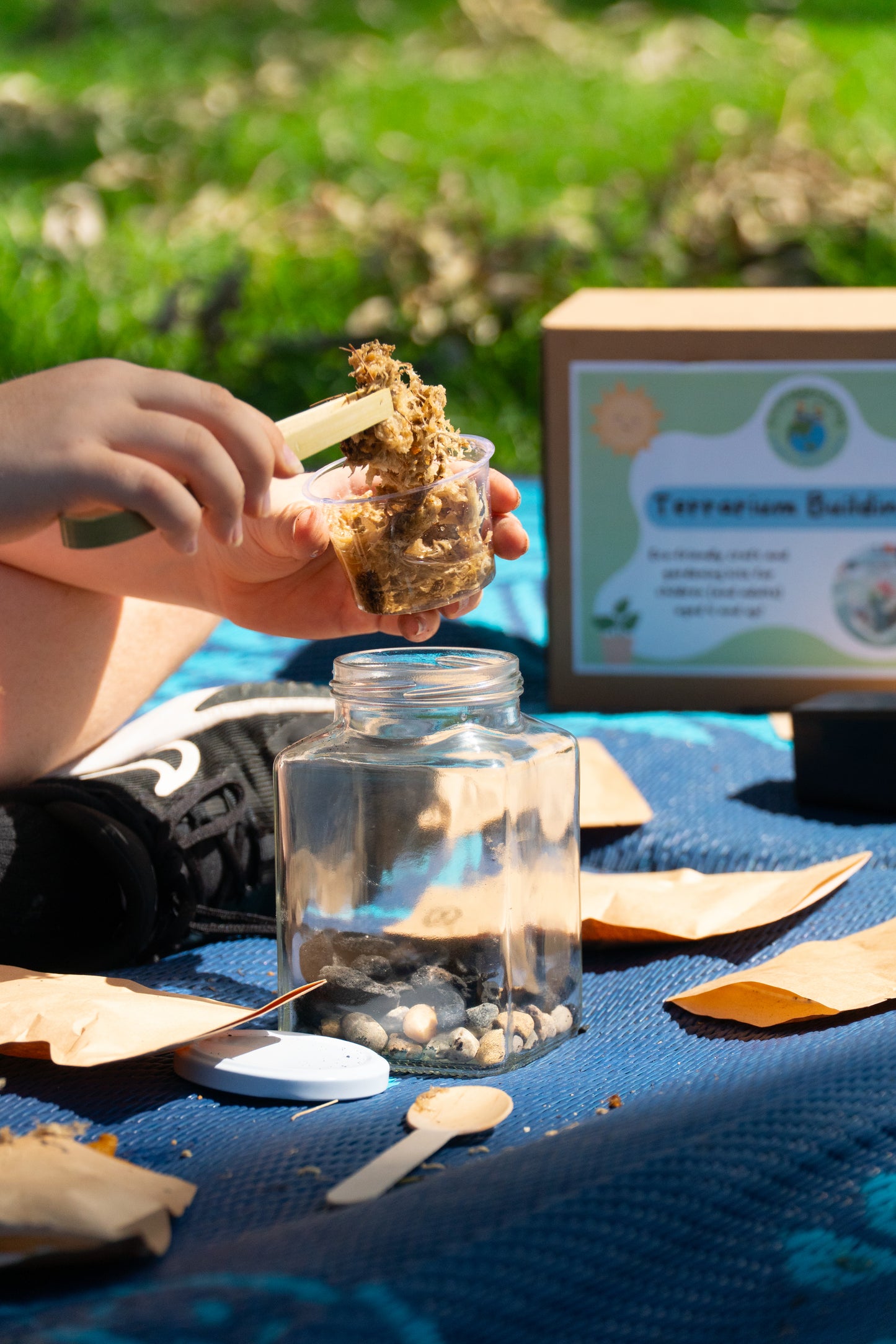 A boy using bamboo tweezers to place his sphagnum moss into his terrarium jar from his EnviroMentoring Terrarium Building DIY kit.