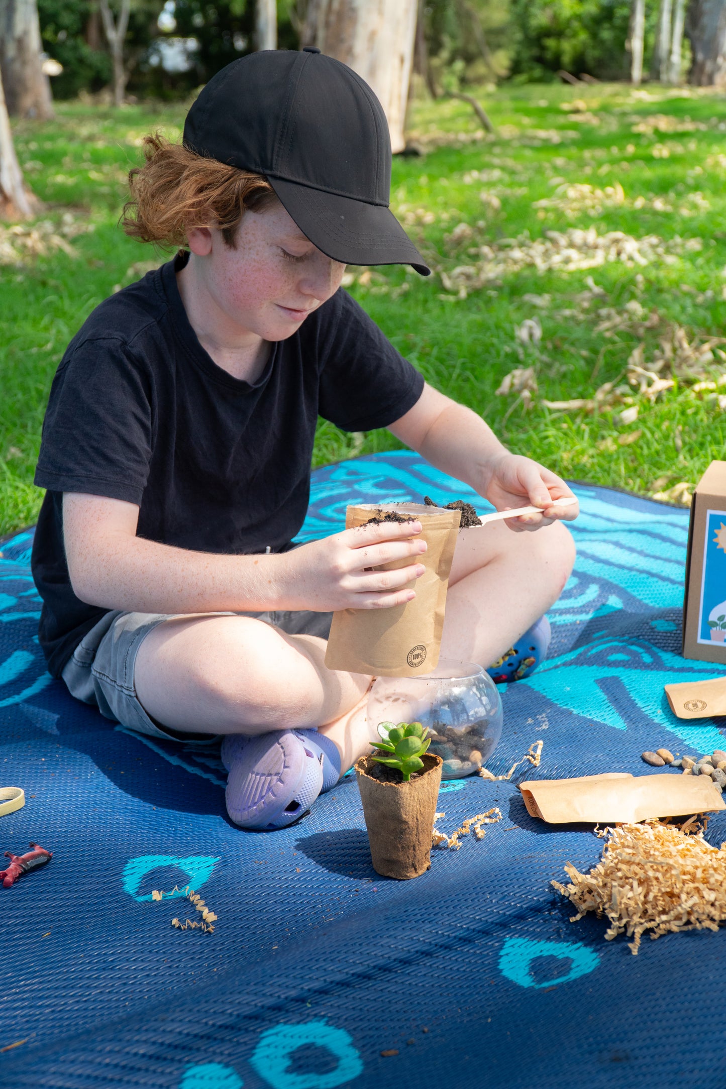 A young boy smiles as he layers his EnviroMentoring Desert Terrarium DIY Kit with soil.