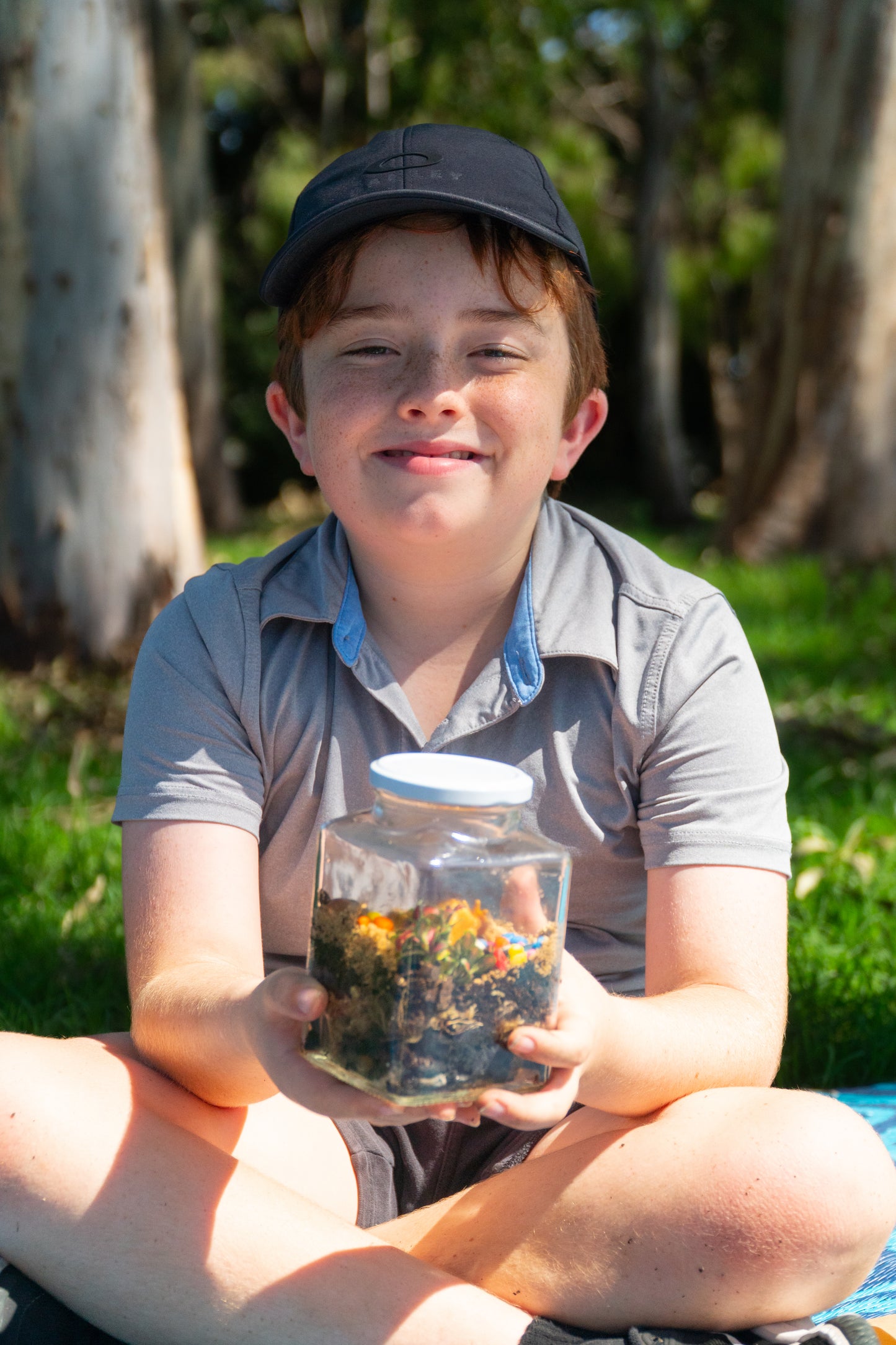 A boy smiling and holding his finished terrarium from the EnviroMentoring Terrarium Building DIY Kit.