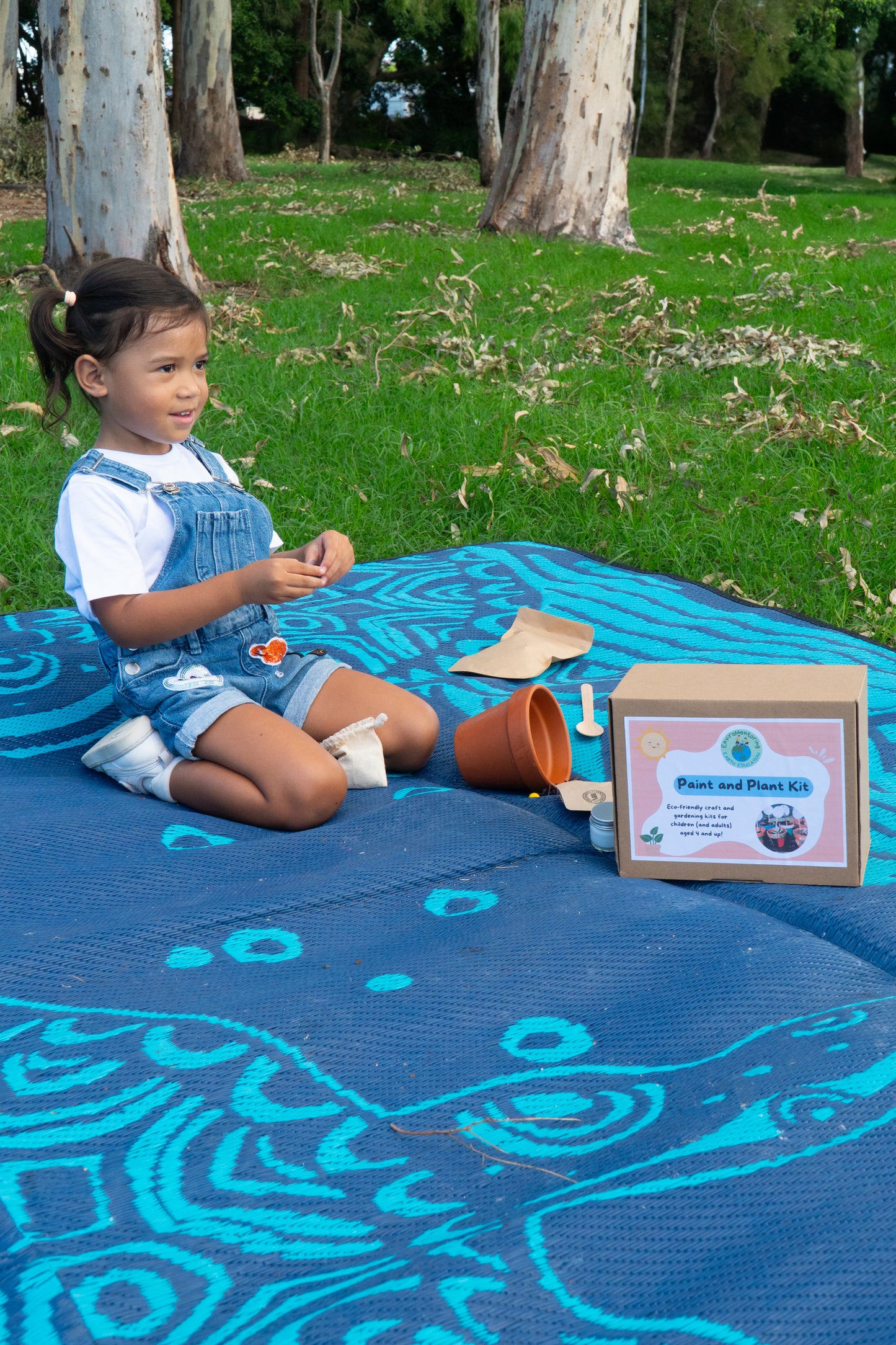 A young girl is smiling at the camera as she decorates her terracotta pot in her EnviroMentoring Paint and Plant DIY Kit.