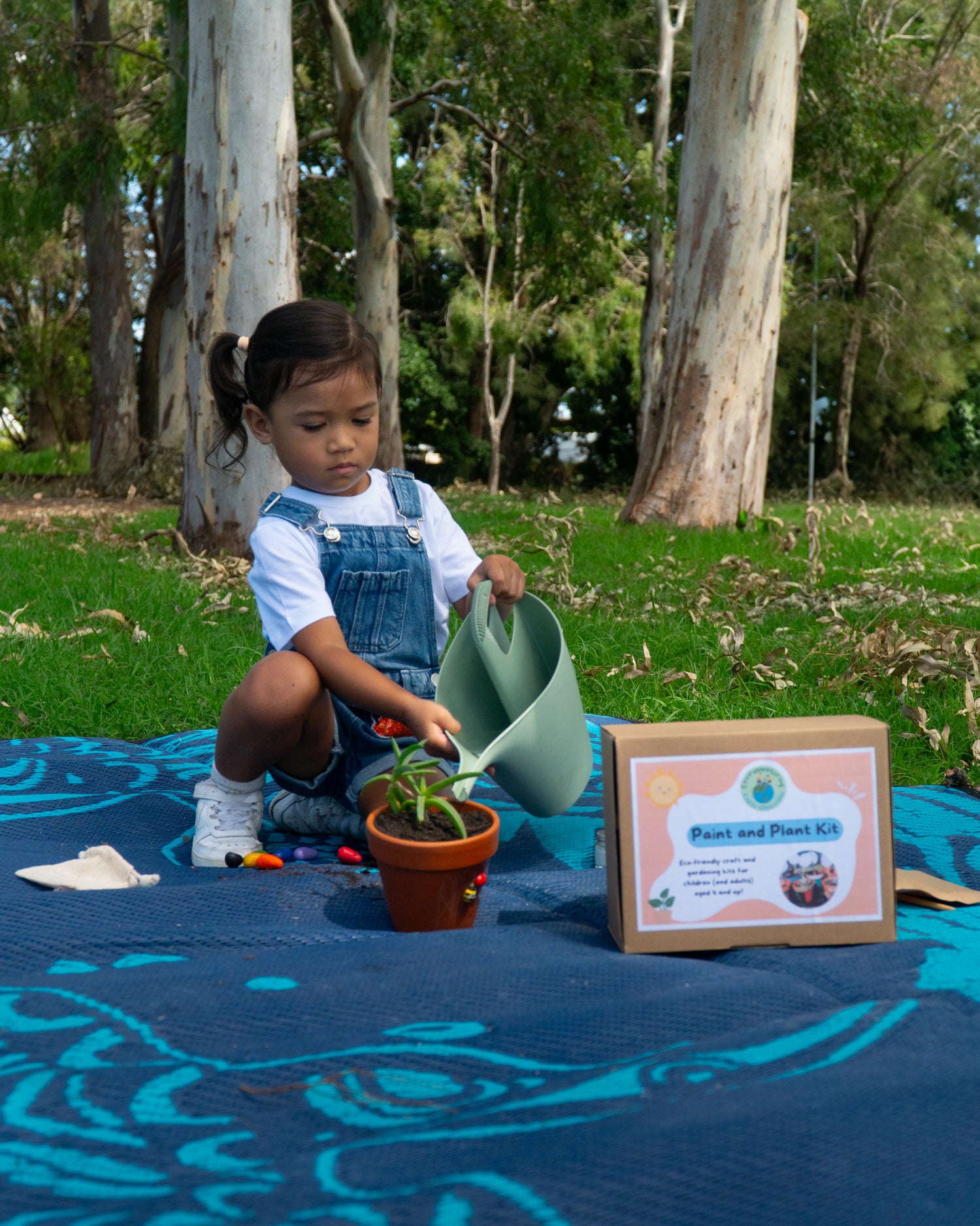 A young girl is watering her completed EnviroMentoring Paint and Plant DIY Kit with a green watering can.