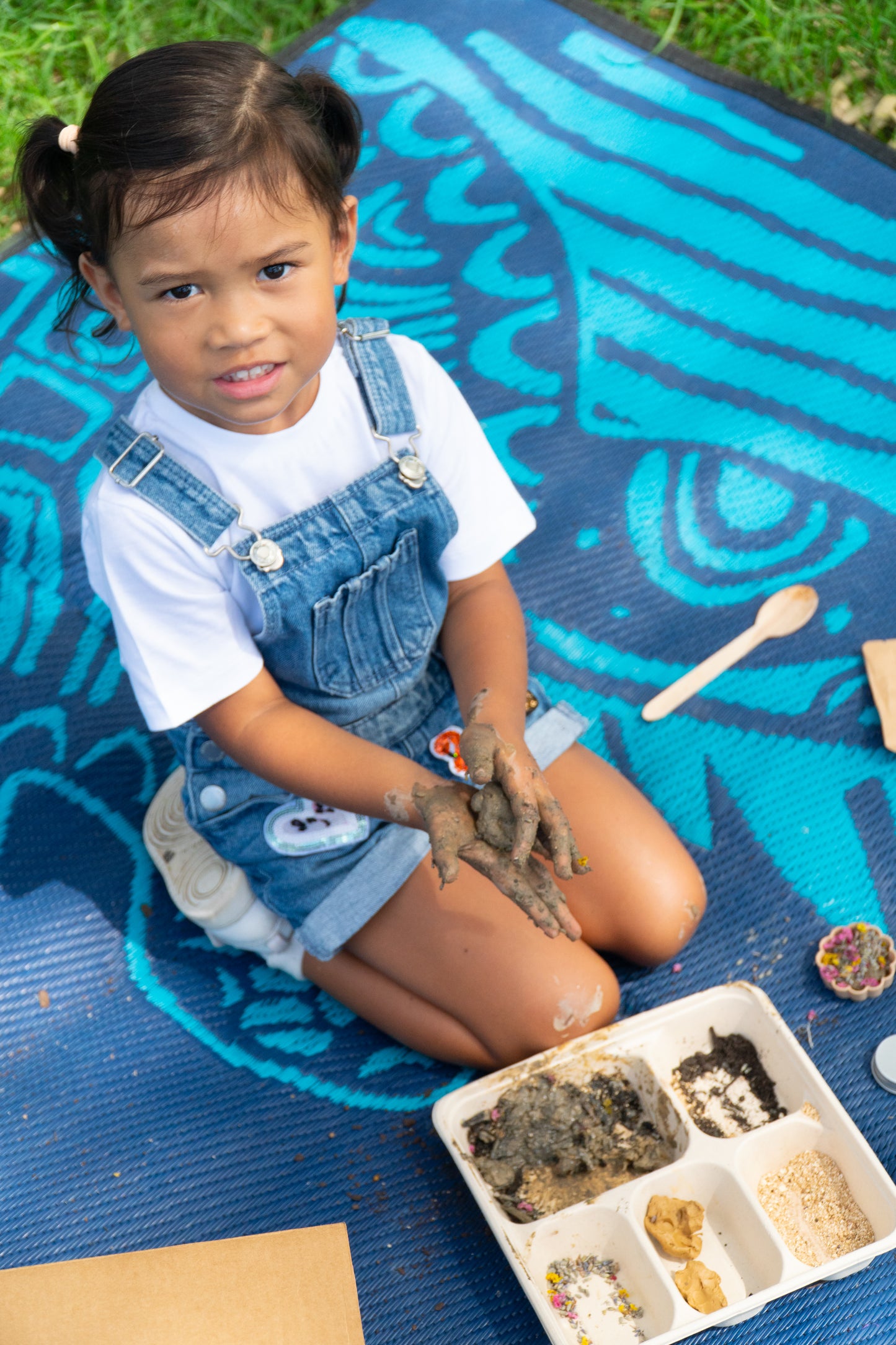 A young girl is smiling up at the camera as she is rolling her EnviroMentoring Seed Surprise DIY Kit into seed surprise shapes.