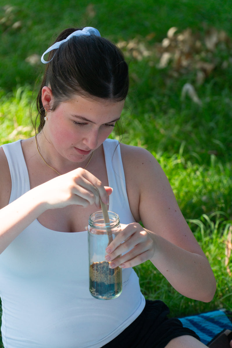 A girl focuses on her EnviroMentoring Wiggly Worms DIY Kit as she flattens the sand layer of her wormery.