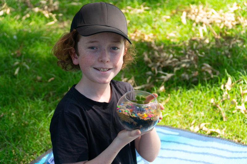 A young boy holds his completed EnviroMentoring Desert Terrarium DIY Kit and smiles.