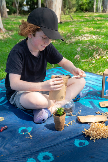 A young boy smiles as he layers his EnviroMentoring Desert Terrarium DIY Kit with soil.
