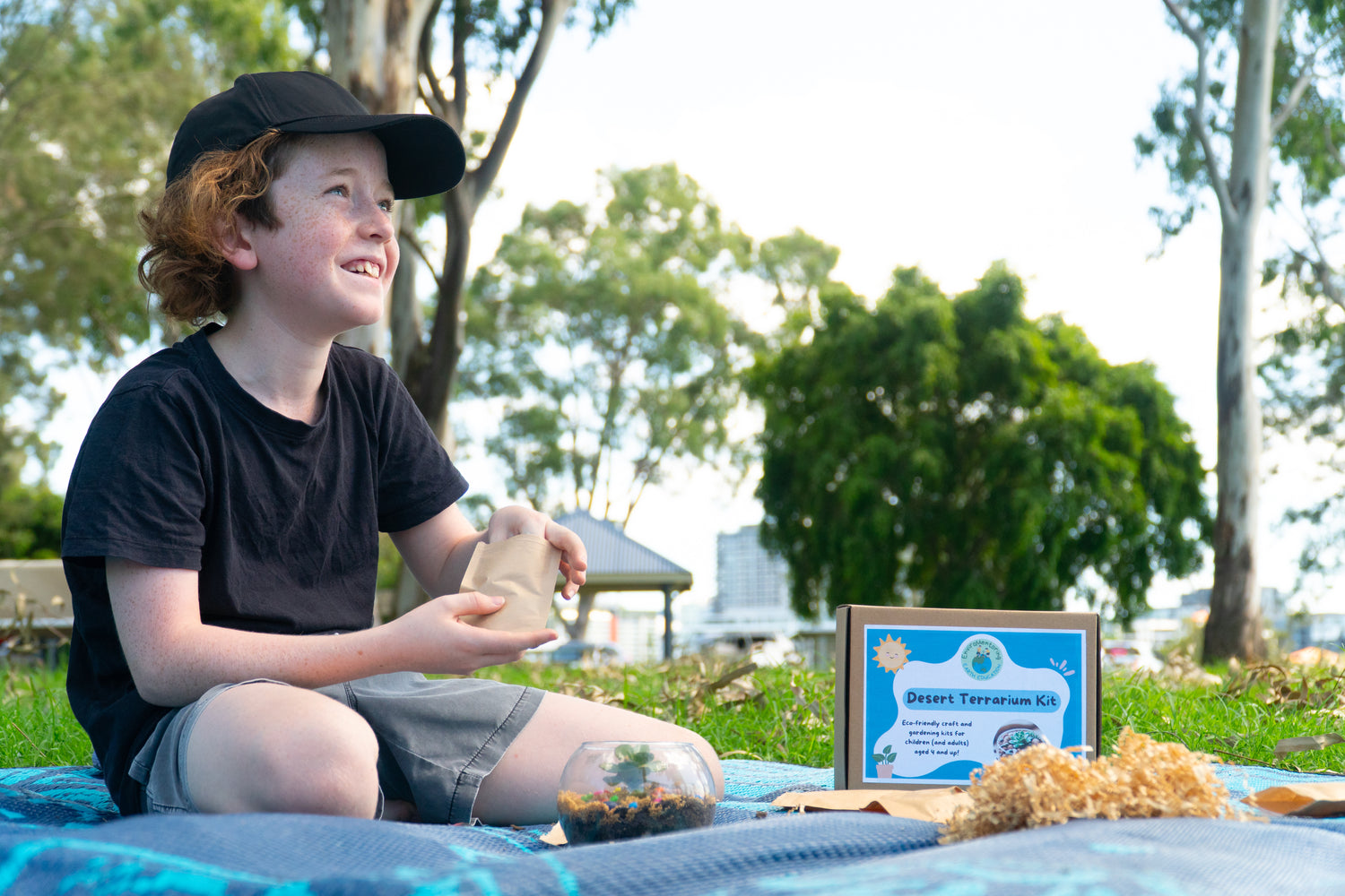 Young boy smiles as he fills his EnviroMentoring Desert Terrarium DIY Kit with rainbow pebbles.